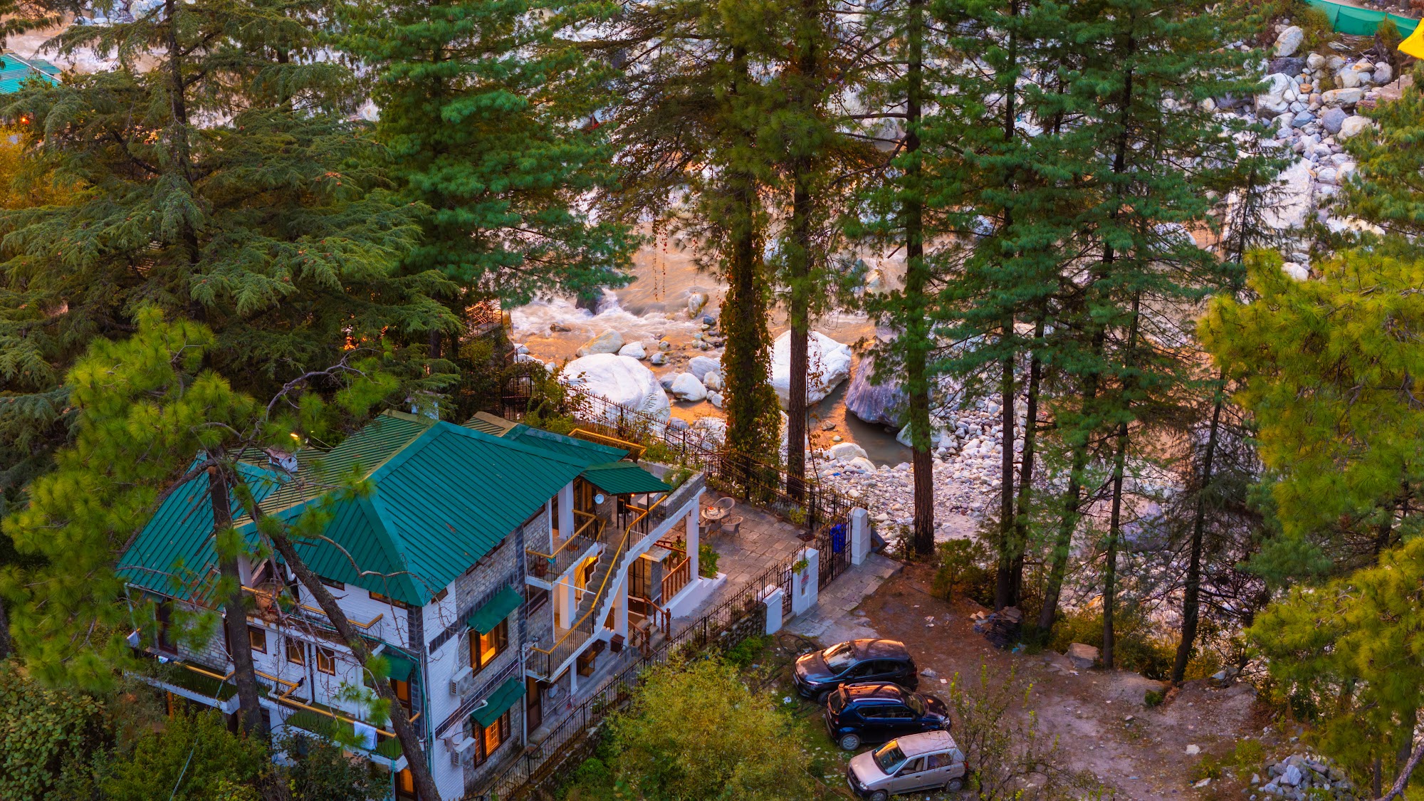 Aerial view of River Stone Villa's green roof among pine trees above the river