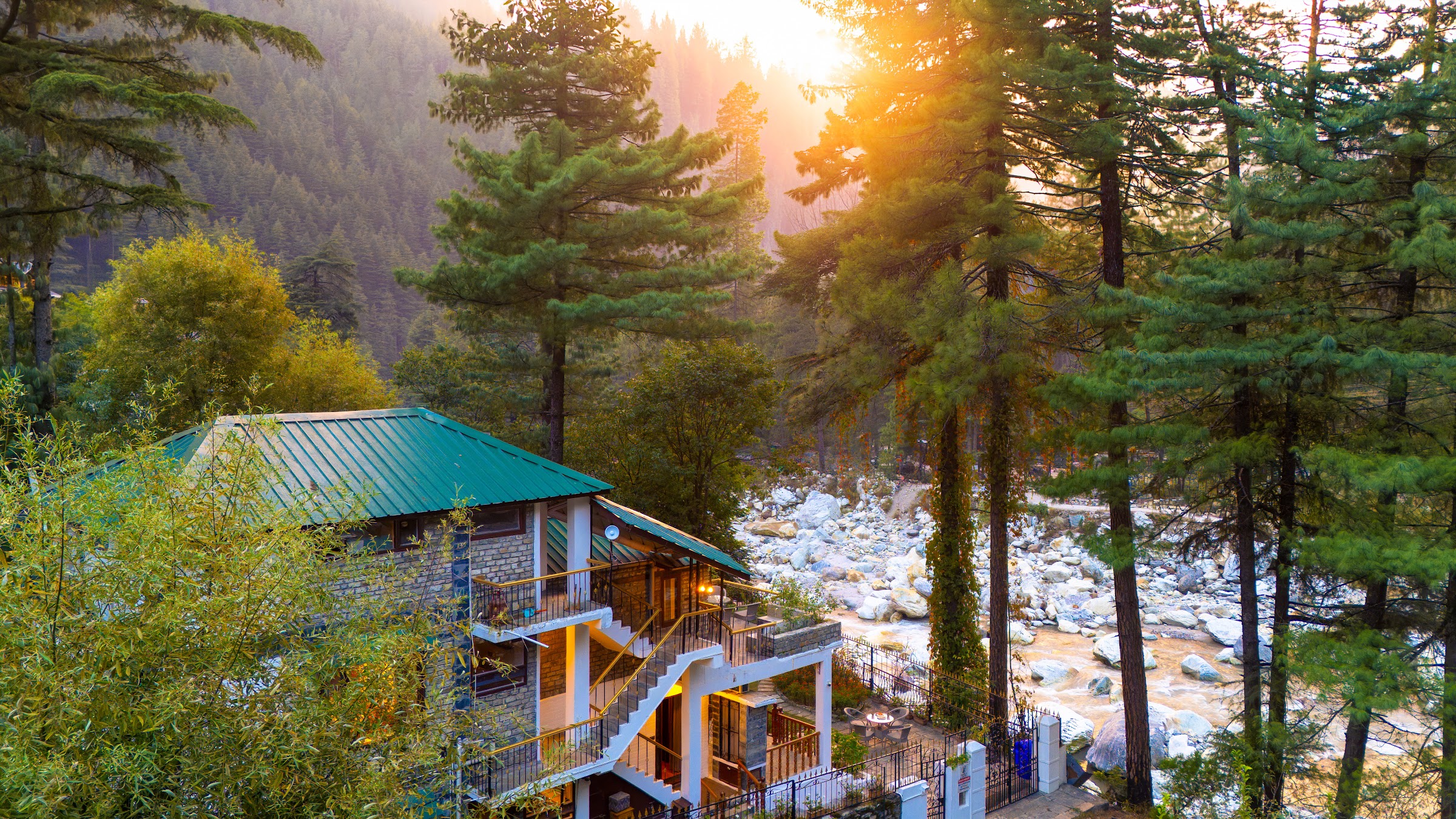 Aerial view of River Stone Villa among pine trees beside the Parvati River in Kasol at sunset